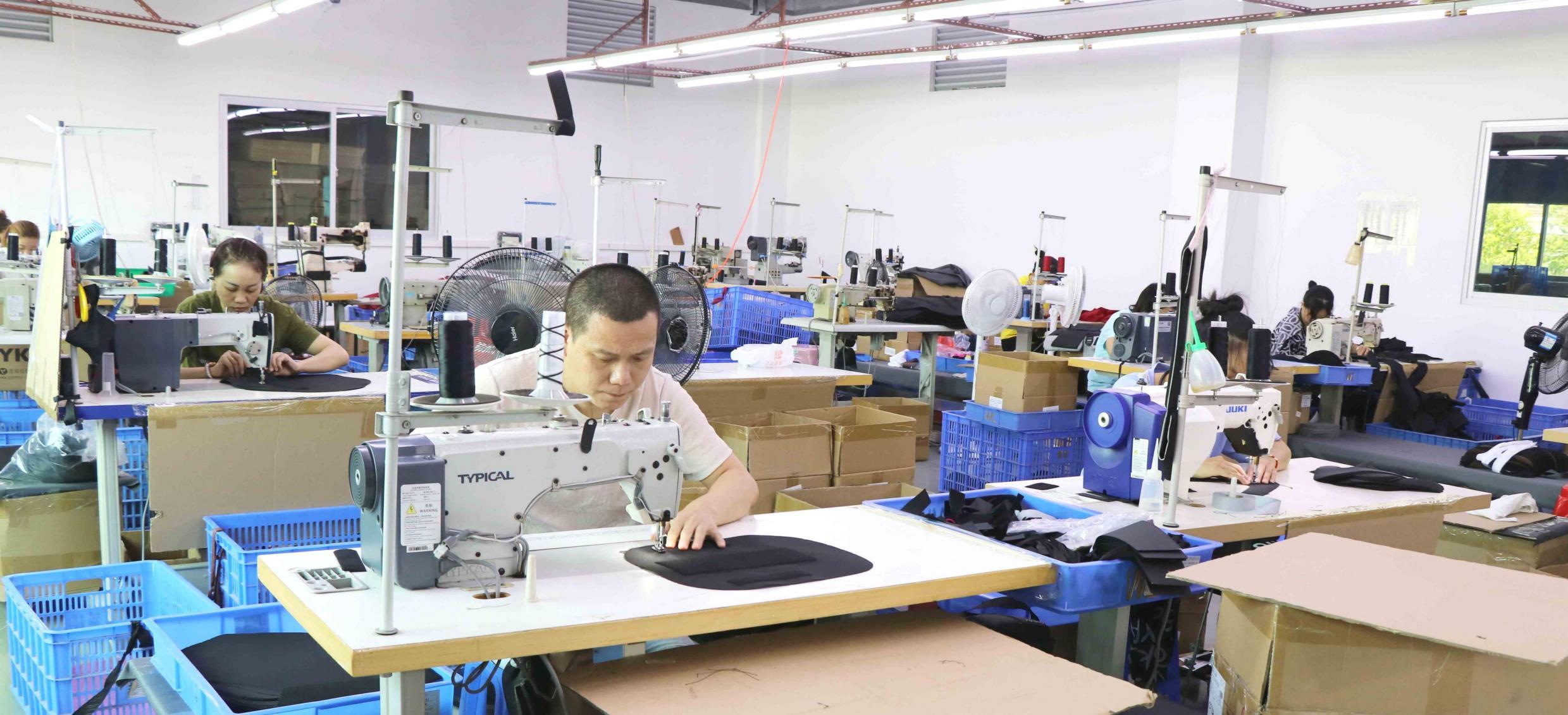 Staff sewing fabric components at industrial sewing machines.